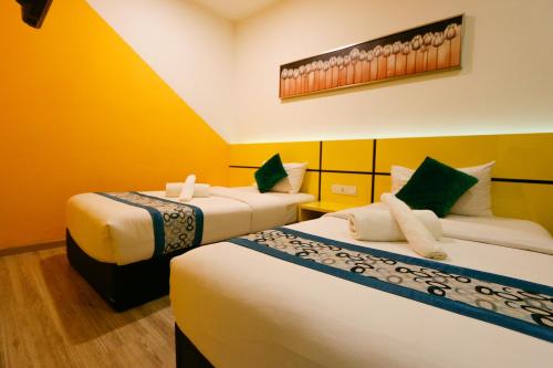 two beds in a room with yellow walls at Golden Roof Hotel Sunway Ipoh in Ipoh