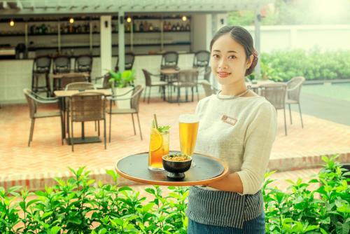 a woman holding a tray with a beer and a drink at Souphattra Hotel Luang Prabang in Luang Prabang