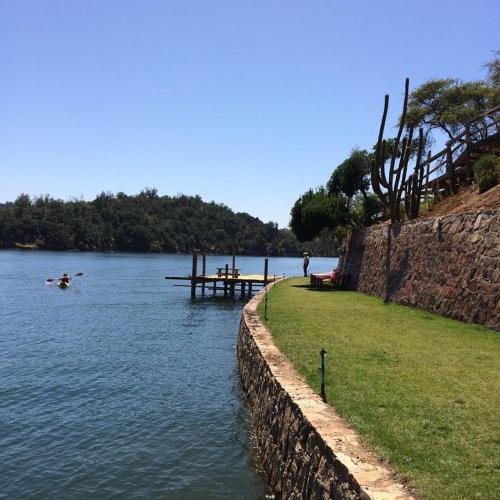 a lake with a dock and a person in a boat at Cabañas Quillay Viejo in Lago Rapel