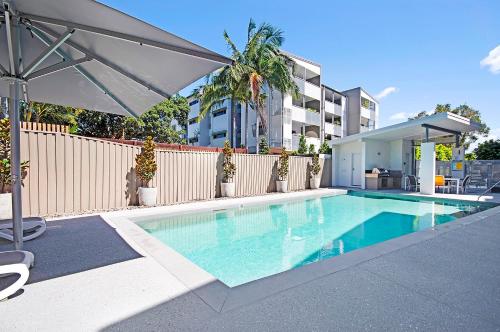 a swimming pool with an umbrella next to a fence at Silver Sea on Sixth Resort in Maroochydore