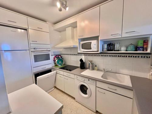 une cuisine avec des armoires blanches et une laveuse et une sécheuse dans l'établissement Appartement confortable avec piscine en bord de mer - FR-1-716-64, au Grau-du-Roi