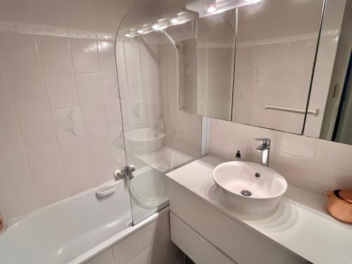 La salle de bains blanche est pourvue d'un lavabo et d'une baignoire. dans l'établissement Appartement confortable avec piscine en bord de mer - FR-1-716-64, au Grau-du-Roi