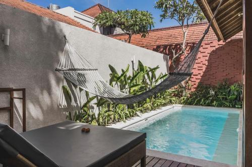 a hammock hanging from a wall next to a swimming pool at Manca Villa Canggu by Ini Vie Hospitality in Canggu