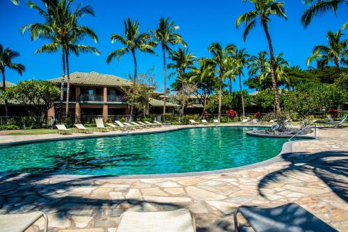 a swimming pool with chairs and palm trees at Fairways402 in Waikoloa