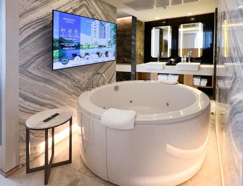 a bathroom with a tub and a tv on a wall at Novotel Rayong Star Convention Centre in Rayong