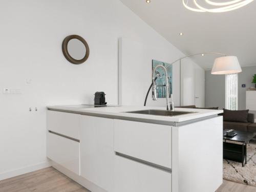 a white kitchen with a sink and a living room at Chalet in Zeeland by Scenic Pond in Wemeldinge