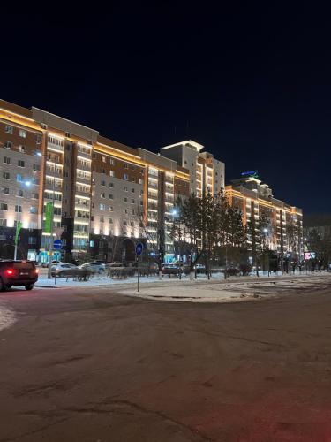 een parkeerplaats voor een gebouw 's nachts bij 215 Рядом с Байтереком для 1-5 чел с 2 большими кроватями и диваном in Astana