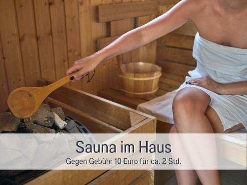 a woman in a sauna holding a wooden spoon at Fewo Herzgrün mit Balkon und Traumblick direkt an Wanderwegen und Sauna im Haus in Todtnauberg