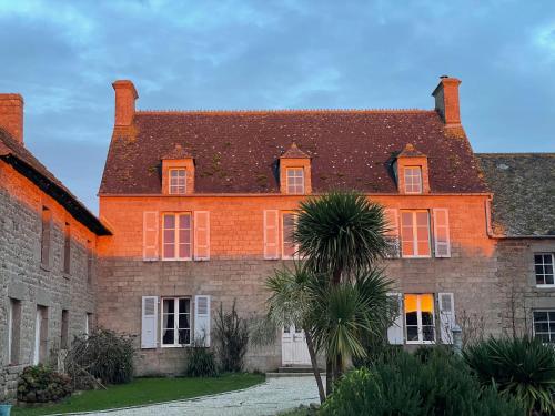 um grande edifício de tijolos com uma palmeira em frente em LA FERME DE NEHOU em Gatteville-le-Phare