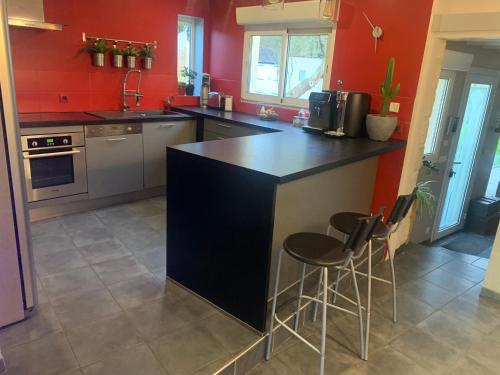 a kitchen with red walls and a black island with stools at Sur les Routes du Débarquement - Chambre Quadruple - in Bavent