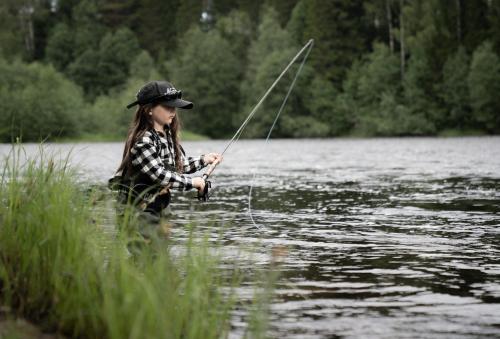 una joven está de pie en un lago de pesca en Cabin by Byske river surrounded by the forest en Byske