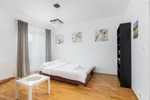 a white bedroom with a bed and a table at Borkowska Comfort Apartment in Krakow