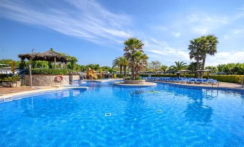 a large blue swimming pool with chairs and palm trees at Camping La Masia - Maeva Vacansoleil in Blanes