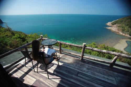 a woman sitting on a deck looking at the ocean at Phangan Utopia Resort in Mae Haad