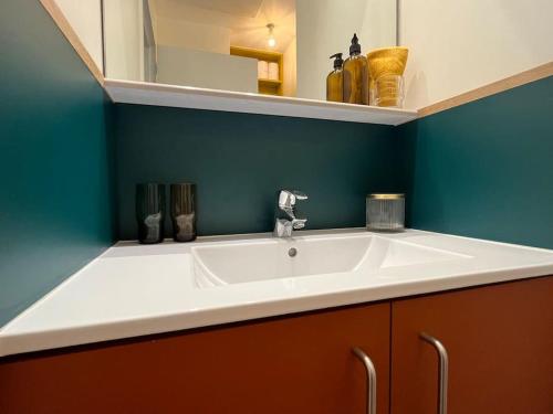 La salle de bains est pourvue d'un lavabo blanc et d'un mur bleu. dans l'établissement CHEVREUIL studio au calme et confortable en centre ville, à Caen