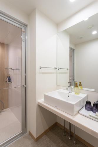 a white bathroom with a sink and a shower at Hotel Sundays Amami in Amami