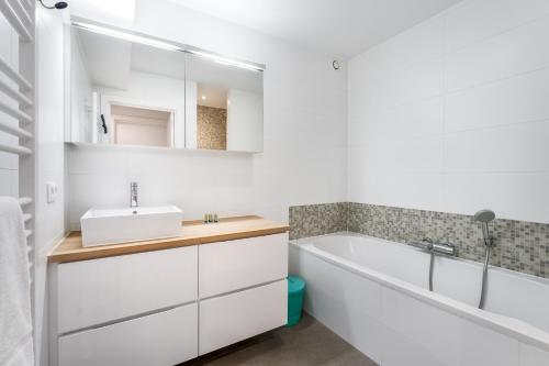 een badkamer met een wit bad en een wastafel bij Lichtrijk & ruim app aan zee met zonneterras - 6p in Wenduine
