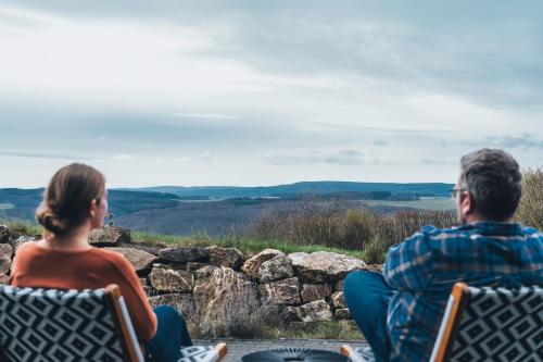 Un uomo e una donna seduti sulle sedie che guardano le colline di Hunsrück Valley View Apartment with Cedar SAUNA a Bruschied