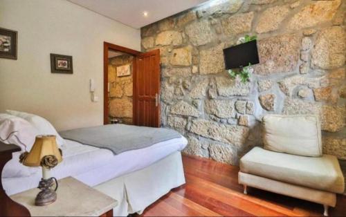 1 dormitorio con pared de piedra, cama y silla en Amazing Flat Sao Bento, en Oporto