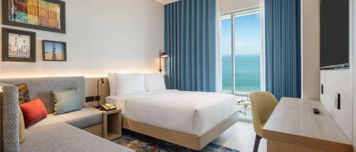 a hotel room with a bed and a couch and a window at Hampton By Hilton Kuwait Salmiya in Kuwait