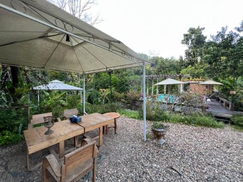 a table and chairs under an umbrella in a garden at Proud Phu Fah Maerim Resort in Mae Rim