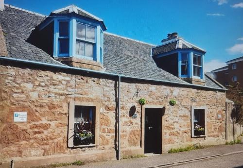 an old stone building with blue windows and a roof at Ness City Cottage - Attic Apartment in Inverness