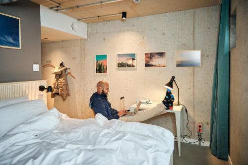 a man sitting on a bed using a laptop at Villa Viva - ein Haus das Brunnen baut in Hamburg