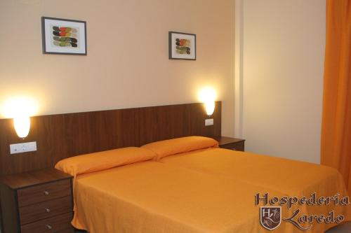 1 Schlafzimmer mit einem Bett mit orangefarbener Bettwäsche und 2 Leuchten in der Unterkunft Hospedería Laredo in La Carlota