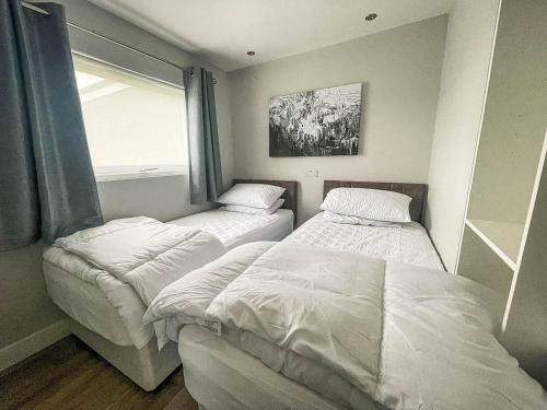 two beds in a small room with a window at Beautiful Chalet In The Seaside Village Of Scratby, Norfolk Ref 51054s in Great Yarmouth