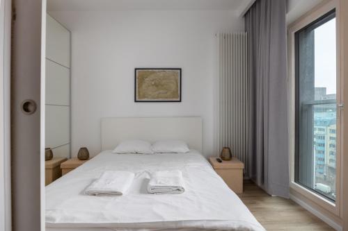a white bedroom with a bed and a large window at VipWarsawApartments Cytryn Mennica Residence in Warsaw