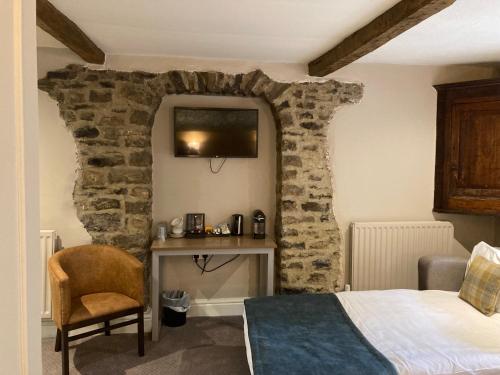 a bedroom with a stone wall with a bed and a desk at Snooty Fox in Kirkby Lonsdale