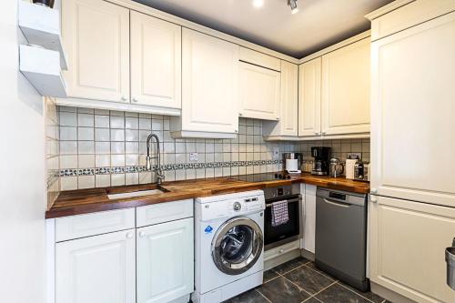 a kitchen with white cabinets and a washer and dryer at Converted Brewery Apartment with Terrace in London