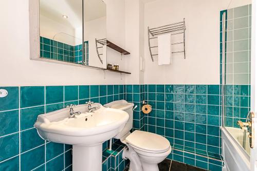a blue tiled bathroom with a sink and a toilet at Converted Brewery Apartment with Terrace in London