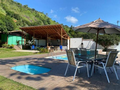 einen Tisch mit Stühlen und einen Sonnenschirm neben einem Pool in der Unterkunft Rancho Vida Boa in Santana do Paraíso