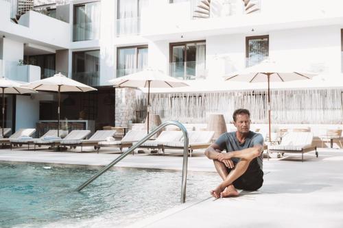 un hombre sentado en el borde de una piscina en Barefoot Hotel Mallorca en Puerto Colom