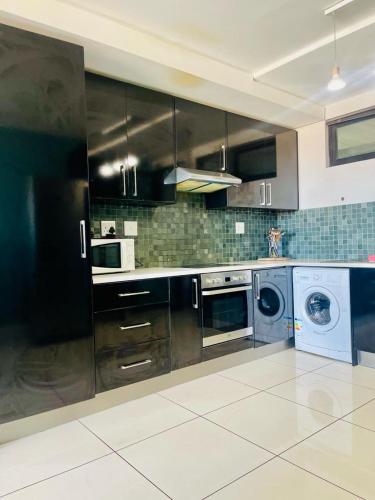 una cocina con armarios negros, lavadora y secadora en 77 Independence Apartment, en Windhoek