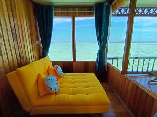 a yellow couch in a room with a view of the ocean at Larapan Water Village 仙本那乐乐棒水屋 in Semporna