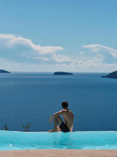 a man sitting on the edge of a swimming pool looking at the ocean at Olvos Luxury Suites in Oia