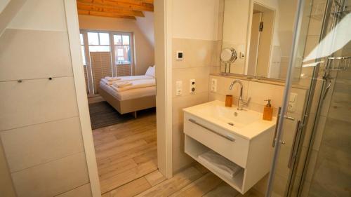 ein Bad mit einem Waschbecken, einem Spiegel und einem Bett in der Unterkunft Fischerhäuschen am Kurpark in Neuharlingersiel