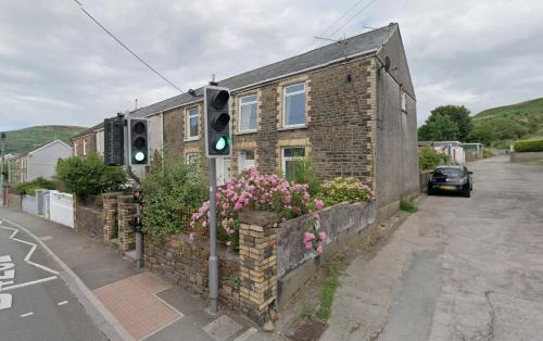 a traffic light in front of a brick house with flowers at Bridgend Rd. Maesteg in Garth