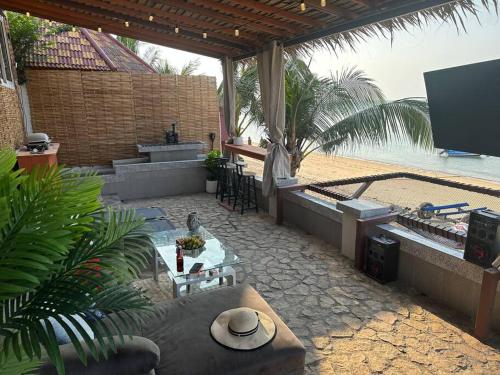 a patio with a table and a tv on the beach at Beach house steps from the sea in Ban Bang Po