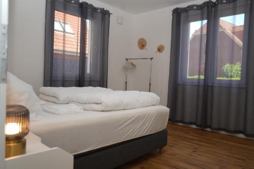 een slaapkamer met een bed met witte lakens en 2 ramen bij Voßgarten Wohnung 1 in Duhnen