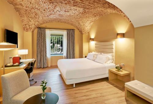 a bedroom with a large white bed and a couch at NH Collection Cáceres Palacio de Oquendo in Cáceres