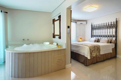 a bathroom with a bath tub next to a bed at Pousada Bora Bora in Bombinhas