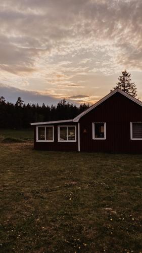 a small black house sitting in a field at Luxurious red cottage with wood stove near lake in Nye