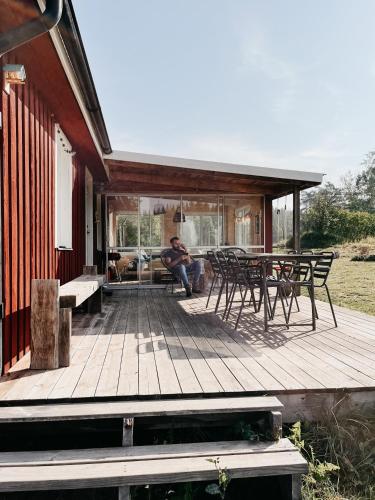 a man sitting on a wooden deck on a house at Luxurious red cottage with wood stove near lake in Nye