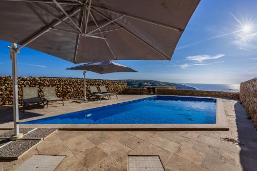 a swimming pool with an umbrella and chairs and a pool at Dwejra Peak House in San Lawrenz
