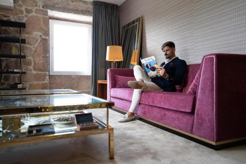 a man sitting on a purple couch reading a book at Quinta da Terrincha in Torre de Moncorvo