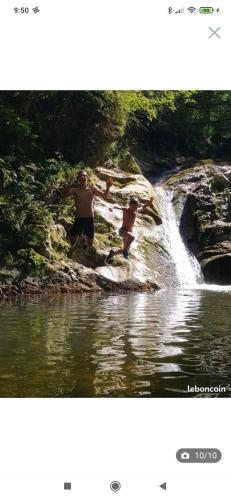 two men are standing in the water near a waterfall at Chez Christian in Le Cheylard