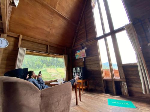 Ein Mann, der auf einer Couch in einem Zimmer mit Fenster sitzt in der Unterkunft Satha private villa Dieng in Banjarnegara